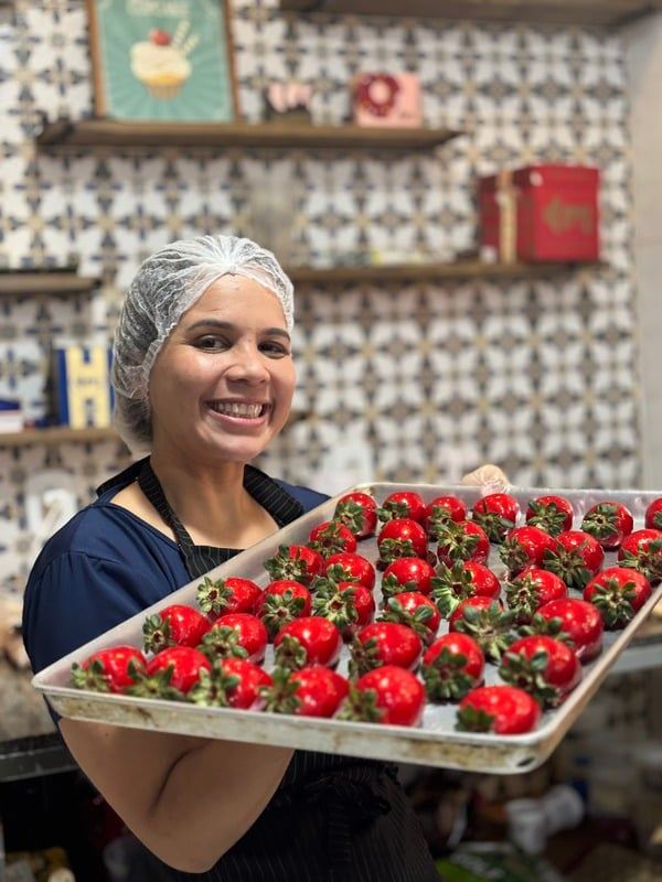 Confeiteira da Doce Mel sorrindo com bandeja de morangos na produção